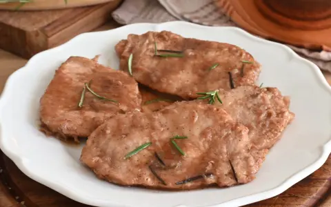 Quattro scaloppine di maiale succulente, guarnite con rosmarino fresco, servite su un piatto bianco.