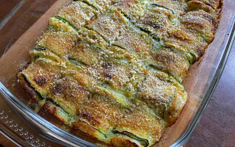 Involtini di zucchine grigliate al forno, dorati e croccanti, in una pirofila di vetro.