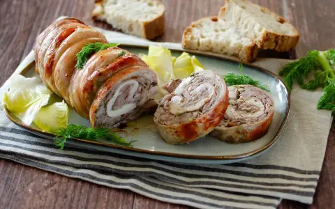 Coniglio in porchetta, un rotolo di carne succulento con erbe aromatiche, servito con pane tostato e insalata.