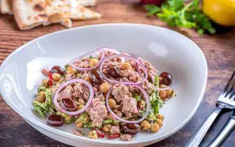 Insalata di ceci e tonno con olive nere e cipolla rossa, servita in un piatto bianco su un tavolo di legno.