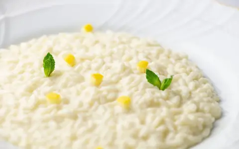Un cremoso risotto al limone, guarnito con cubetti di limone e foglie di menta fresca, su un piatto bianco.