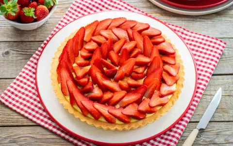 Deliziosa crostata di fragole con crema pasticcera, decorata con fragole fresche affettate. Un dolce estivo perfetto.