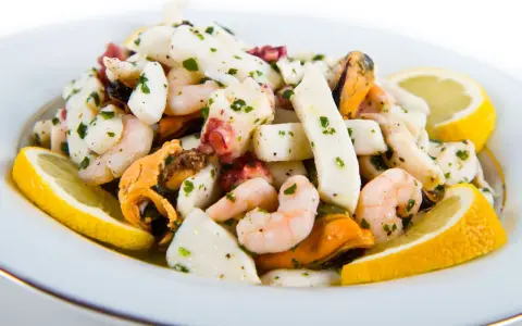 Deliziosa insalata di mare con verdure, gamberi, calamari, polpo e cozze, guarnita con spicchi di limone fresco e prezzemolo tritato.
