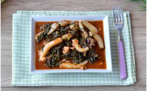 Un saporito piatto di seppie in zimino, con verdure scure e salsa rossa, servito su un tovagliolo a quadretti verdi.