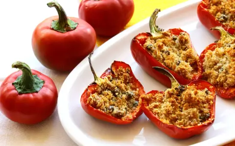 Peperoni ripieni di tonno e pangrattato, dorati e invitanti, su un piatto bianco.