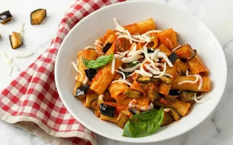 Piatto di pasta alla norma con melanzane fritte, pomodoro, basilico e ricotta salata grattugiata.