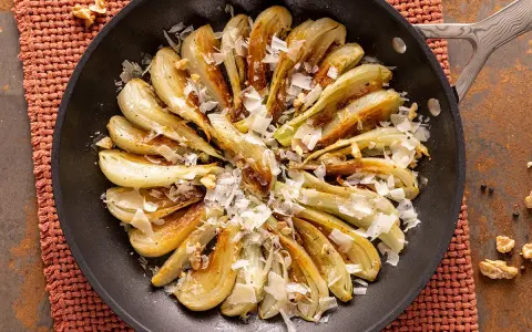 Finocchi in padella dorati, guarniti con scaglie di formaggio e noci croccanti. Un contorno saporito e invitante.