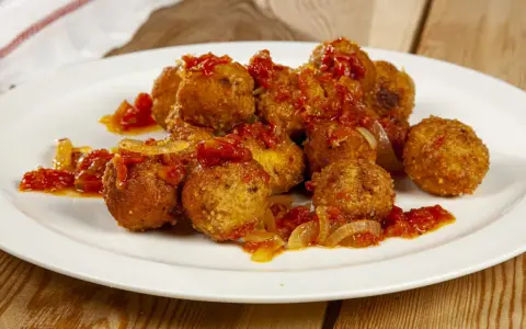 Polpette di pesce dorate e saporite, condite con un sugo rosso di pomodoro e cipolla, servite su un piatto bianco.