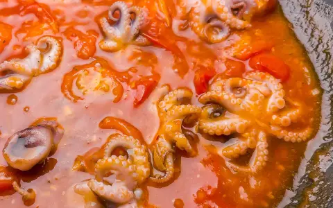Piccolo polpo alla luciana in un sugo rosso ricco, con tentacoli visibili e pomodorini.