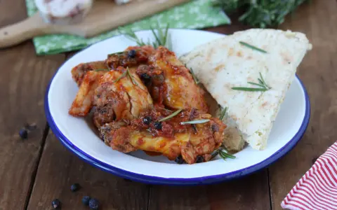 Piatto di friccò di pollo succulento con rosmarino e pane rustico su un piatto smaltato.