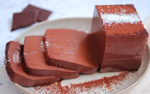 Fette di budino al cioccolato, spolverate di cacao e cocco, su un piatto.