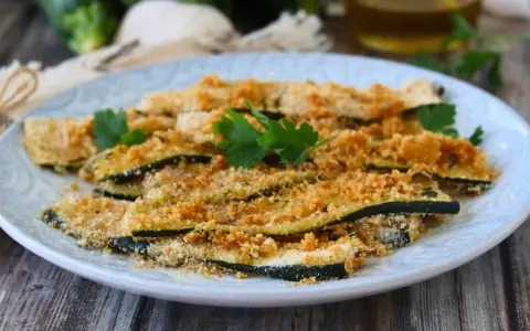 Fette di zucchine al forno, impanate e dorate, guarnite con prezzemolo fresco. Un contorno leggero e gustoso.