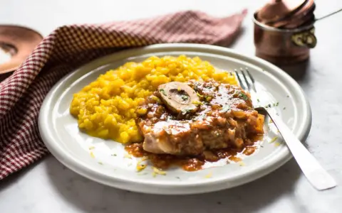 Un succulento ossobuco alla milanese, con il suo midollo invitante, adagiato su un letto di risotto giallo zafferano.