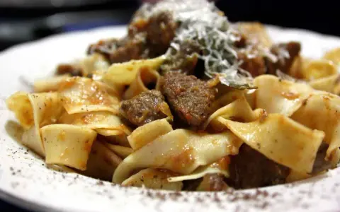 Pappardelle al cinghiale, un piatto ricco e saporito con pasta fresca e ragù di cinghiale, spolverato di parmigiano.