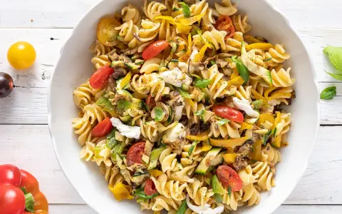 Un piatto invitante di pasta fredda saporita con fusilli, pomodorini, zucchine, peperoni gialli e mozzarella.