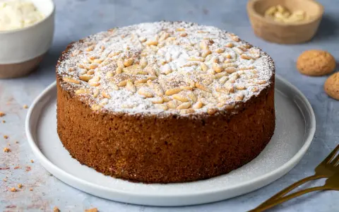 Torta soffice con farina di mandorle, guarnita con pinoli e zucchero a velo. Perfetta per ogni occasione.