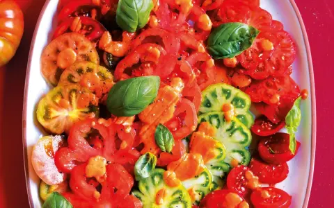 Un'insalata di pomodori colorati, affettati e conditi con erbe aromatiche fresche.