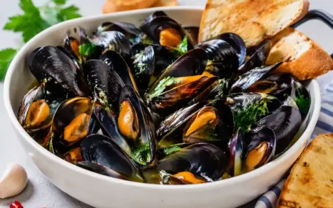 Soute di cozze fumante in una ciotola bianca, guarnita con prezzemolo fresco e accompagnata da fette di pane tostato.
