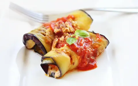 Deliziosi involtini di melanzane ripieni, conditi con sugo di pomodoro e basilico fresco, pronti per essere gustati.