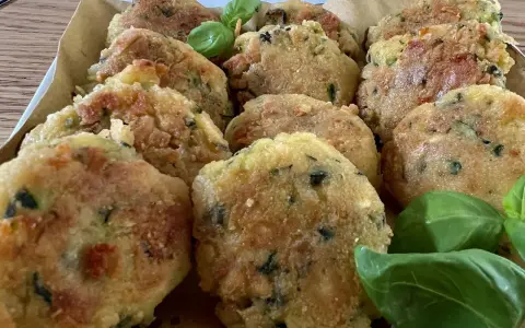 Deliziose polpette di zucchine grattugiate in padella, dorate e croccanti, guarnite con foglie di basilico fresco.