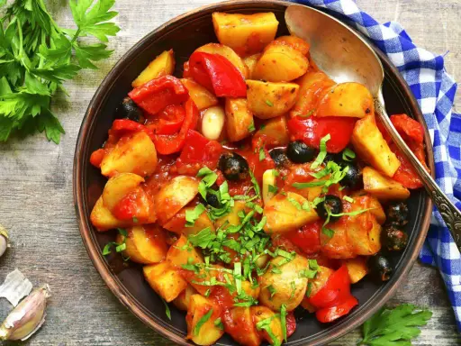 Patate e peperoni in padella, un piatto saporito con olive nere e prezzemolo fresco.
