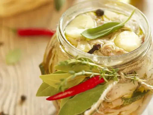 Tonno di coniglio in olio, con erbe aromatiche, peperoncino e spezie, in un barattolo di vetro decorato con spago.