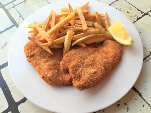Due cotolette di pollo dorate e croccanti, accompagnate da patatine fritte e uno spicchio di limone.