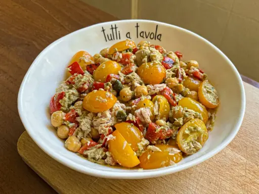 Insalata di tonno con pomodorini gialli, ceci e peperoni rossi, condita con un pesto leggero. Perfetta per un pasto fresco e gustoso.