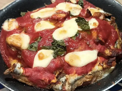 Parmigiana di alici in teglia, con pomodoro, mozzarella filante e basilico. Un piatto saporito e invitante.