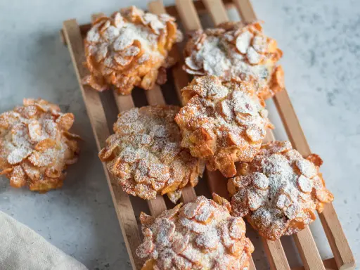 Deliziose rose del deserto, dolcetti croccanti ricoperti di fiocchi di mais e spolverati di zucchero a velo, su un tagliere di legno.