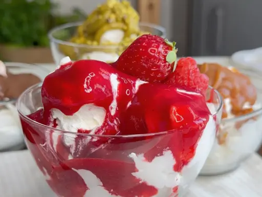 Coppetta di gelato alla fragola, con fragole fresche e salsa rossa. Scopri come fare il gelato senza gelatiera per un dessert delizioso.