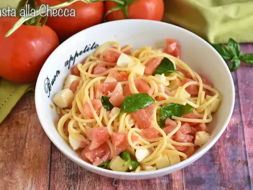 Un piatto di pasta alla checca con pomodori freschi, mozzarella e basilico, pronto per essere gustato.