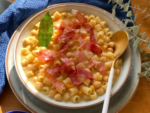 Un piatto fumante di pasta e ceci, guarnito con prosciutto crudo e una foglia di alloro.