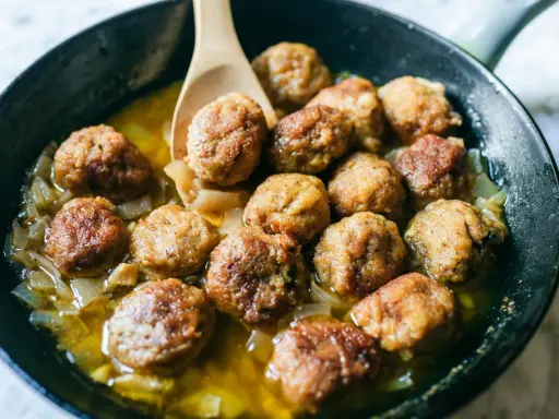 Polpette di carne morbide in padella, dorate e succulente, cuociono in un sughetto saporito con cipolle.