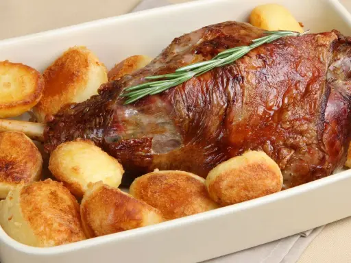 Un succulento agnello al forno con patate arrosto dorate, guarnito con un rametto di rosmarino fresco.