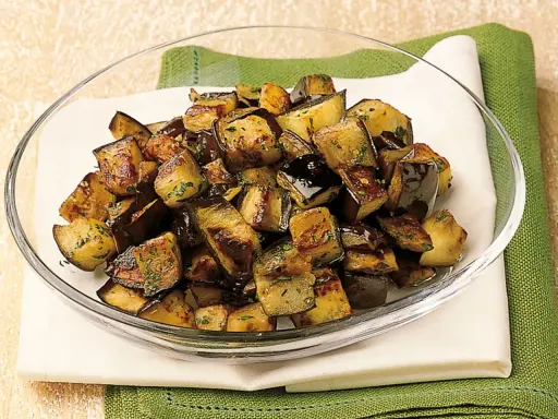 Melanzane a funghetto dorate e saporite, condite con erbe aromatiche, servite in una ciotola di vetro.