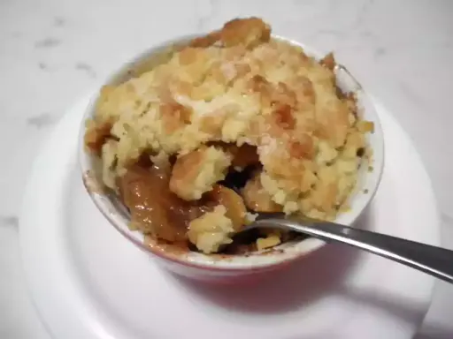 Un delizioso crumble di mele appena sfornato, con la sua crosta dorata e il ripieno succoso, pronto per essere gustato con un cucchiaino.