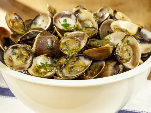 Un invitante sautè di vongole, condito con prezzemolo fresco e olio d'oliva, servito in una ciotola bianca su un tavolo di legno.