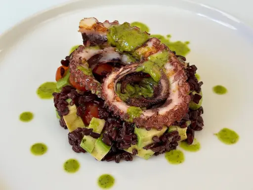 Delizioso polpo alla griglia su letto di riso venere, avocado e pomodorini, condito con salsa verde.