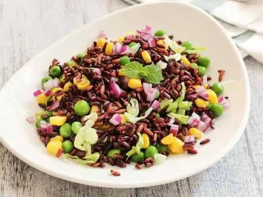 Insalata di riso Venere colorata con piselli, mais, cipolla rossa e lattuga croccante, guarnita con menta fresca.