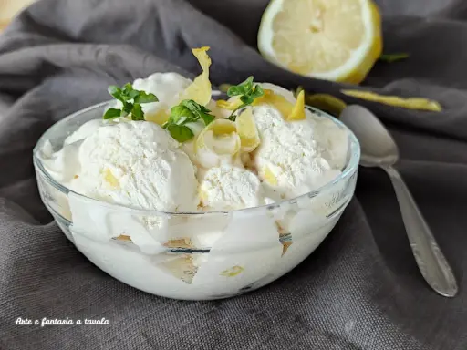 Coppa di cremoso gelato al limone, guarnita con scorzette e foglioline di menta. Un limone fresco sullo sfondo.