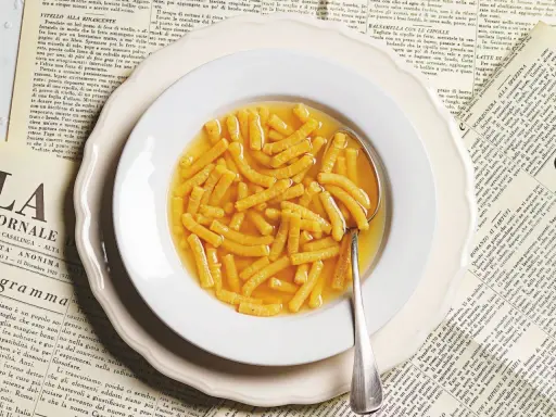 Passatelli in brodo, un classico della ricetta italiana, serviti in un piatto bianco su vecchie pagine di giornale.