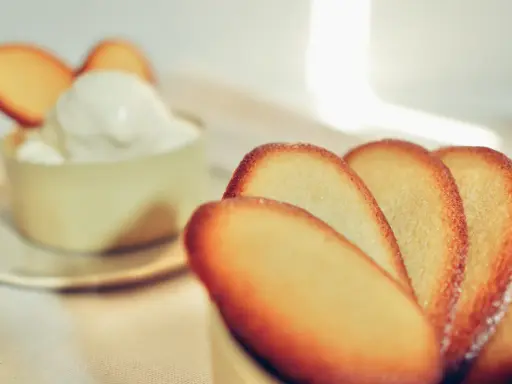 Biscotti croccanti a forma di lingue di gatto, alcuni in primo piano, altri decorano una coppa di panna montata.