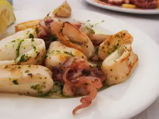 Calamari in padella, succulenti e dorati, conditi con prezzemolo fresco e serviti con una fetta di limone.