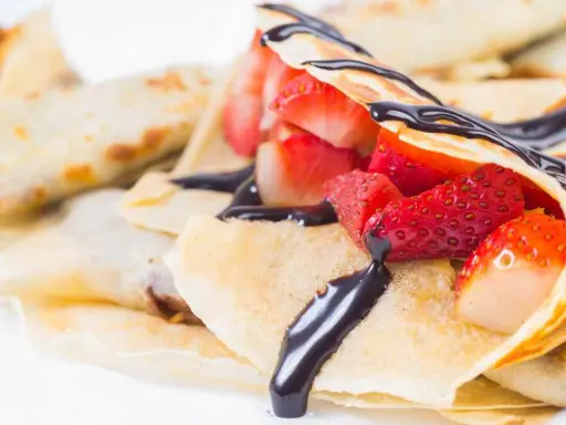 Deliziose crepes senza burro, ripiene di fragole fresche e ricoperte da una cascata di cioccolato fondente.