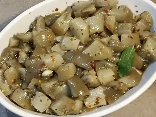 Un invitante piatto di insalata di melanzane, condita con olio, aglio e peperoncino, guarnita con una fogliolina di menta.