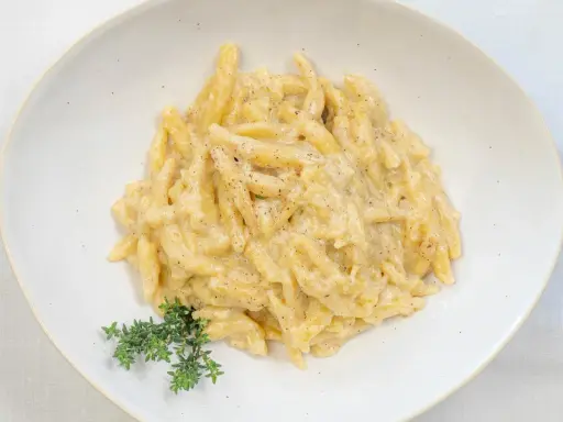 Ravioles val Varaita, pasta fresca condita con una cremosa salsa al formaggio e pepe nero, guarnita con timo fresco.