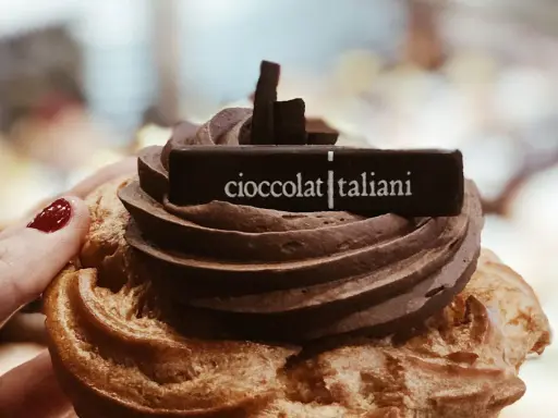 Una mano con smalto rosso tiene un delizioso dolce al cioccolato, decorato con la scritta "cioccolatitaliani".