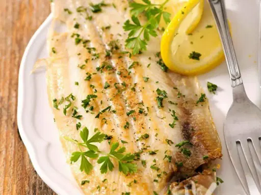 Sogliola al forno, dorata e profumata, guarnita con prezzemolo fresco e spicchi di limone. Un piatto leggero e saporito.