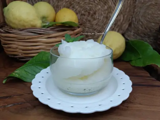 Granita al limone fatta in casa, fresca e dissetante, servita in una coppetta con foglioline di menta. Limoni freschi in un cesto sullo sfondo.